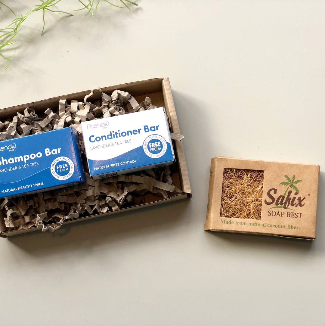 Natural shampoo and conditioner bars with a coconut fibre soap rest packaged in a brown kraft gift box with shredded paper. 